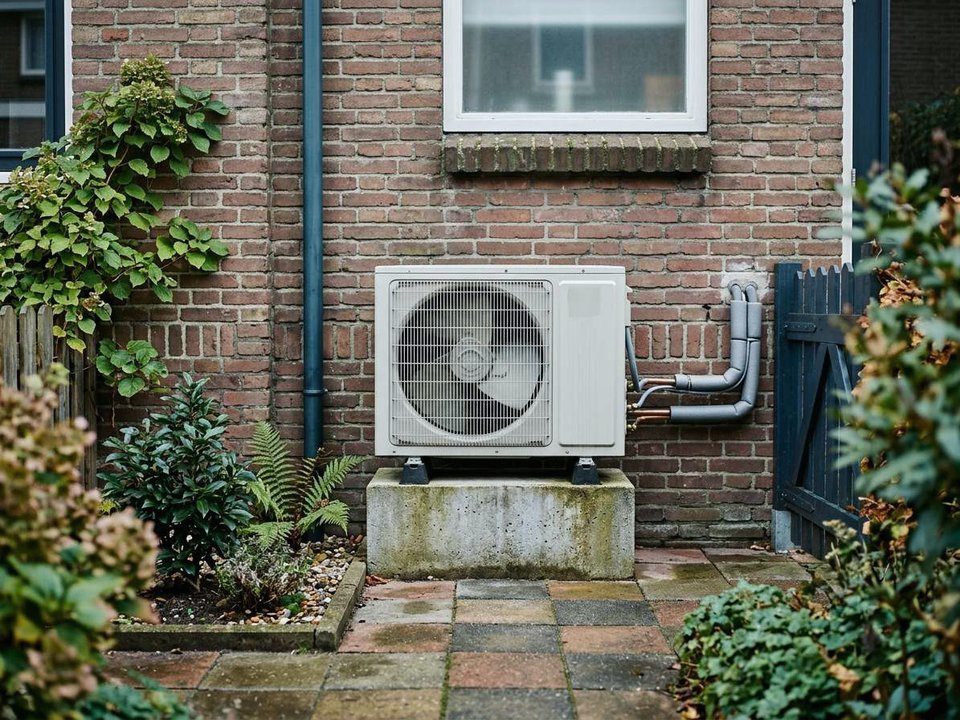Buitenunit van een warmtepomp tegen de bakstenen achtergevel van een woning